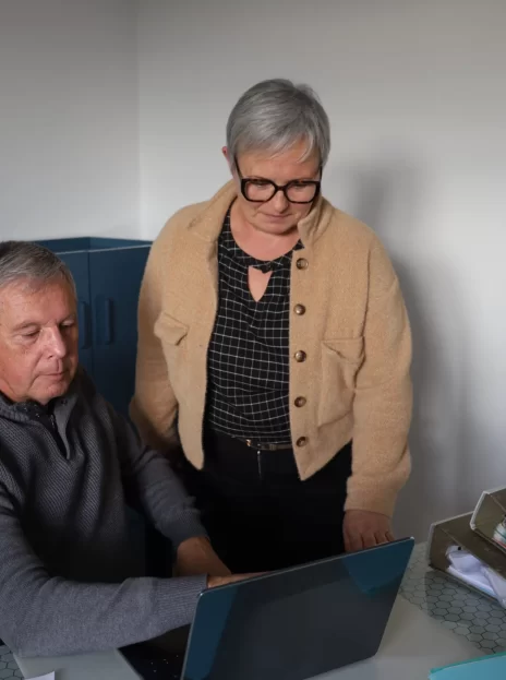 Un jeune créateur d’entreprise assis à son bureau avec les mains sur sa souris d’ordinateur et sourit avec un expert Dixit facile qui se tient à côté.